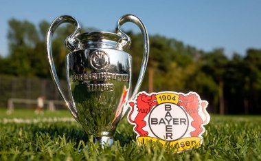 30 Ağustos 2021, Leverkusen, Almanya. Bayer 04 Leverkusen futbol kulübü amblemi ve yeşil çimenli UEFA Şampiyonlar Ligi Kupası.