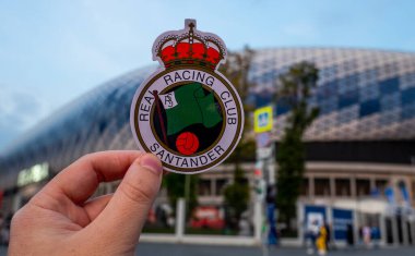 12 Eylül 2021, Santander, İspanya. Racing de Santander futbol kulübünün amblemi modern bir stadyumun arka planına karşı..