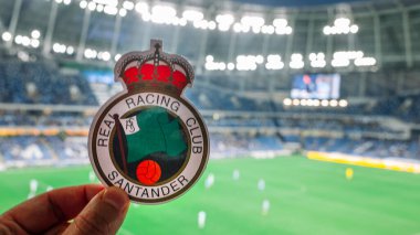 12 Eylül 2021, Santander, İspanya. Racing de Santander futbol kulübünün amblemi modern bir stadyumun arka planına karşı..