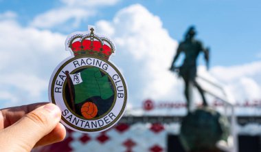 14 Haziran 2021, Santander, İspanya. Racing de Santander futbol kulübünün amblemi modern bir stadyumun arka planına karşı..