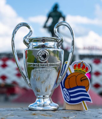 14 Haziran 2021, San Sebastian, İspanya. Real Sociedad futbol kulübünün amblemi ve UEFA Şampiyonlar Ligi Kupası modern bir stadyumun arka planına karşı..