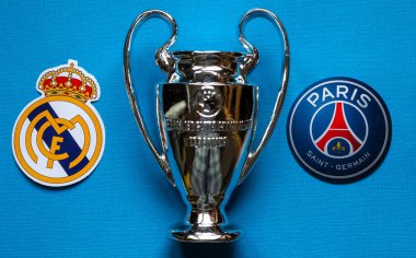19 Aralık 2021 St. Petersburg, Rusya. UEFA Şampiyonlar Ligi 'nin 1 / 8 finallerinin futbol kulüplerinin amblemleri Paris Saint-Germain F.C. Real Madrid CF ve mavi arka planda bir fincan..