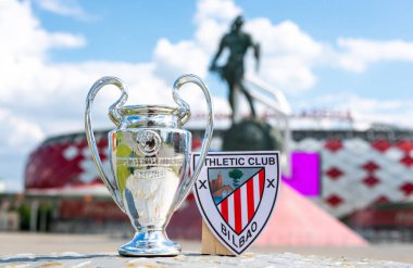 14 Haziran 2021 Bilbao, İspanya. Futbol kulübü Athletic Bilbao 'nun amblemi ve UEFA Şampiyonlar Ligi Kupası modern bir stadyumun arka planına karşı.