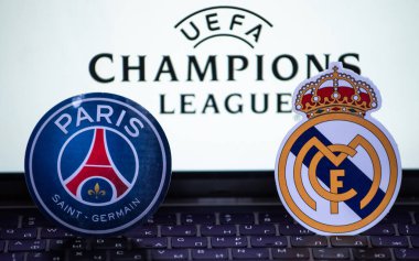 2 Ocak 2022 St. Petersburg, Rusya. UEFA Şampiyonlar Ligi 'nin 1 / 8 finallerinin futbol kulüplerinin amblemleri Paris Saint-Germain F.C. ve Real Madrid CF turnuva ambleminin arka planında.