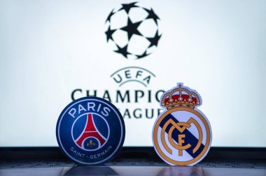 2 Ocak 2022 St. Petersburg, Rusya. UEFA Şampiyonlar Ligi 'nin 1 / 8 finallerinin futbol kulüplerinin amblemleri Paris Saint-Germain F.C. ve Real Madrid CF turnuva ambleminin arka planında.
