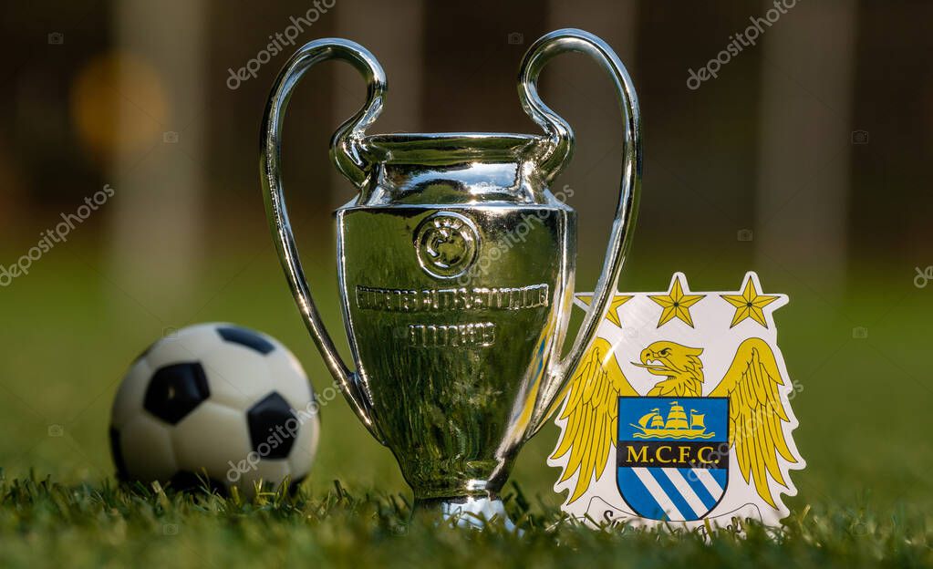 August 27, 2021, Manchester, United Kingdom. The emblem of Manchester City football club and the UEFA Champions League Cup on the green lawn of the stadium.