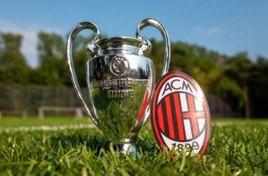 30 Ağustos 2021, Milan, İtalya. Modern bir stadyumun arka planında A.C. Milan futbol kulübü ve UEFA Şampiyonlar Ligi Kupası amblemi yer almaktadır..