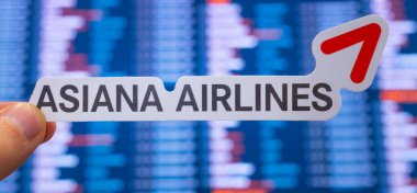 11 Aralık 2021, Seul, Güney Kore. Havayolu şirketi Asiana Airlines 'ın arkaplanındaki amblemi ve uluslararası havaalanındaki uçuş tarifesi..