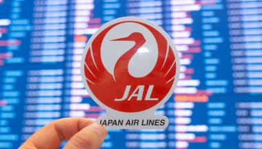 11 Aralık 2021, Tokyo, Japonya. Japon Hava Yolları, uluslararası havaalanındaki uçuş çizelgeleriyle elektronik bir panonun arka planına karşı amblem oluşturuyor..