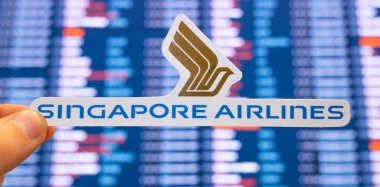 11 Aralık 2021, Singapur. Singapur Havayolları 'nın amblemi, uluslararası havaalanındaki uçuş çizelgeleriyle birlikte elektronik bir skorbordun arka planına karşı..