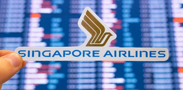 11 Aralık 2021, Singapur. Singapur Havayolları 'nın amblemi, uluslararası havaalanındaki uçuş çizelgeleriyle birlikte elektronik bir skorbordun arka planına karşı..