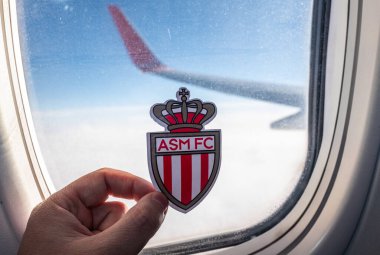 6 Aralık 2021. Monaco 'da. Uçak penceresinin arka planında AS Monaco FC futbol kulübünün amblemi.