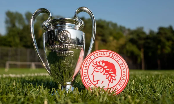 30 Ağustos 2021 Atina, Yunanistan. Futbol kulübü Olympiacos Pire 'nin amblemi ve yeşil çimenli UEFA Şampiyonlar Ligi Kupası.