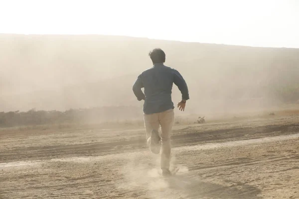 Rear view of a Man running away on dusty road