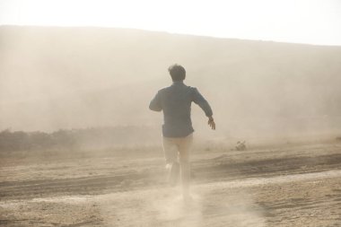 Tozlu yolda koşan bir adamın arka görüntüsü