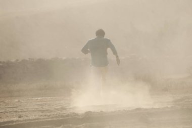 Tozlu yolda koşan bir adamın arka görüntüsü