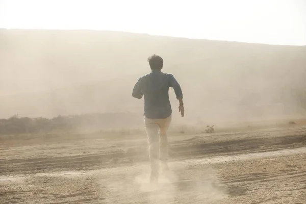 Rear view of a Man running away on dusty road