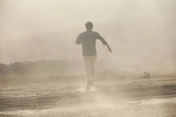 Rear view of a Man running away on dusty road