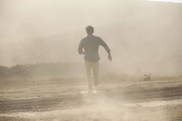 Rear view of a Man running away on dusty road