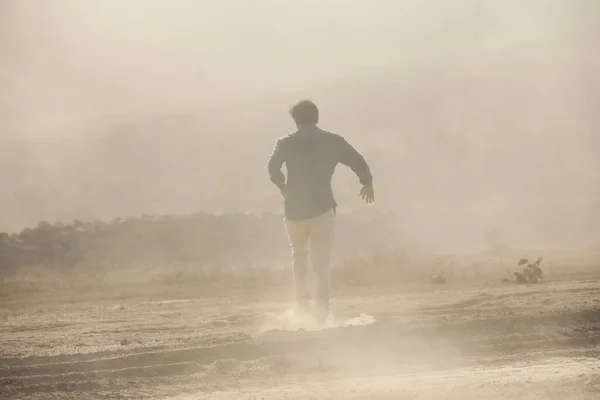 Rear view of a Man running away on dusty road