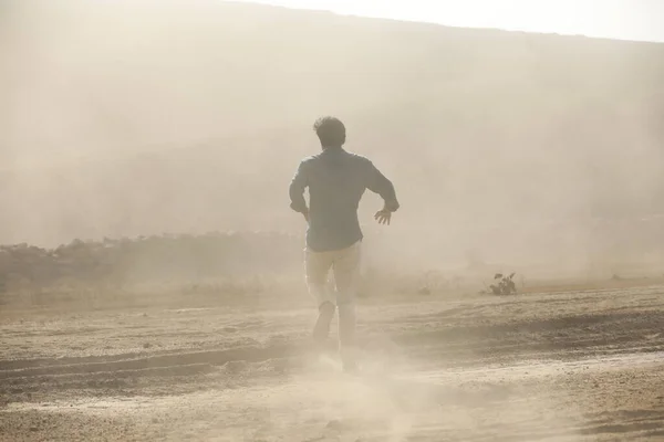 Rear view of a Man running away on dusty road