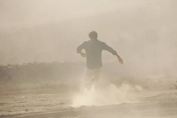 Rear view of a Man running away on dusty road