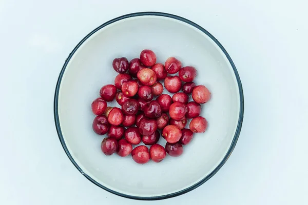 Many red cherry fruits with drops in round bowl, isolated on white. Organic berries fresh. A lot of sweet cherries without petioles top view