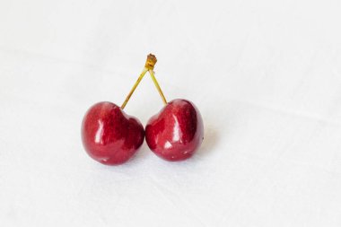 Two juicy berries of a red cherry on a white fabric background. Couple of red juicy cherries with stems. Two red connected sweet cherries, tasty and ripe fruit