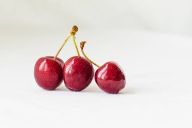 Three juicy berries of a red cherry on a white fabric background. Couple of red juicy cherries with stems. Two red connected sweet cherries, tasty and ripe fruit