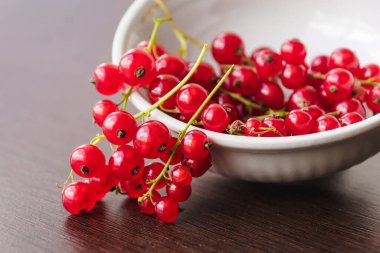 Sprigs of red currant in a white bowl closeup. Sweet red currant spilling out from the bowl. Currant organic berries harvest - healthy eating and food concept