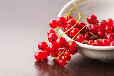 Sprigs of red currant in a white bowl closeup. Sweet red currant spilling out from the bowl. Currant organic berries harvest - healthy eating and food concept