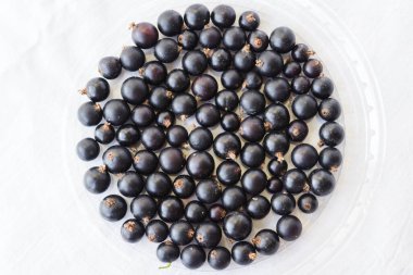 Black berries on white. Blackcurrants in a transparent bowl isolated on a white background. Blackcurrant with copy space for text. Top view berries closeup.