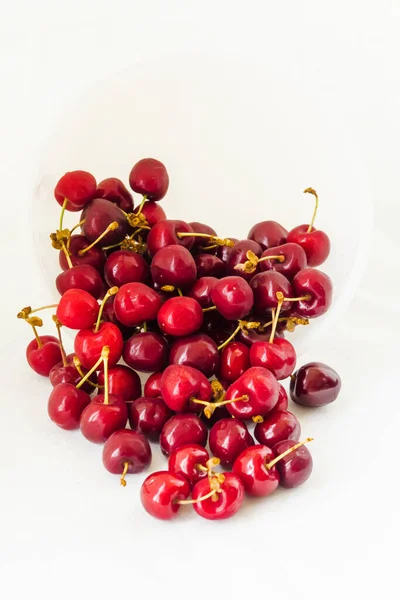 Many sweet cherries closeup vertically. Red cherries on a white fabric background. Juicy organic red cherries for jam, juice, smoothies, compote, desserts and cakes. Healthy eating and food concept