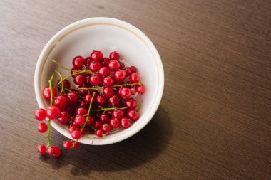 Sprigs of red currant in a white bowl closeup top view. Sweet red currant spilling out from the bowl. Currant organic berries harvest - healthy eating and food concept