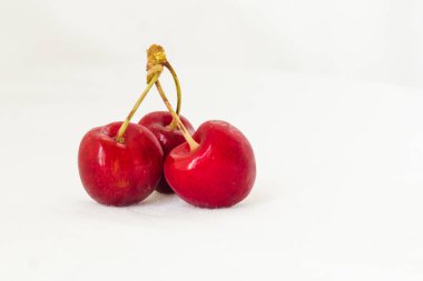 Three juicy berries of a red cherry on a white fabric background. Few red juicy cherries with stems. Two red connected sweet cherries, and one single cherry next to them. Delicious and ripe fruits