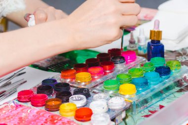 Boyalı çok renkli kavanozlar. Boyalı resmin işleyişi. Resim stüdyosunda fırça tutan kadın sanatçının elleri. Yaşam tarzı ve hobi kavramı