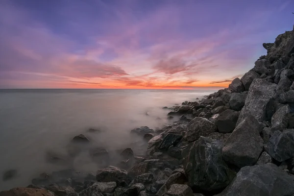 Pôr do sol sobre uma praia rochosa Fotos De Bancos De Imagens