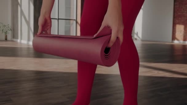Jeune femme déploie tapis de sport rouge dans un studio de yoga spacieux close-up. — Video