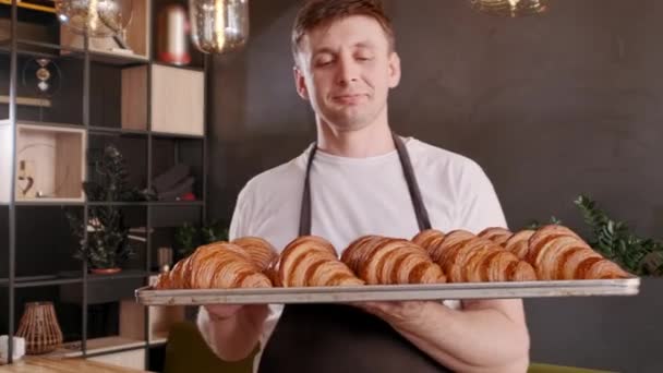 Baker harapás öntözés frissen sült francia croissant vett sütőlap. Vidám pék — Stock videók