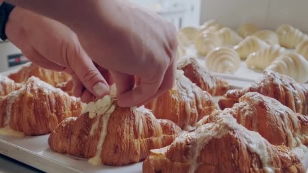 Croissant s mandlovými vločkami. Pekař zdobí čerstvé zlaté croissanty s mandlovými vločkami — Stock video