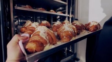 Baker pişirmek için fırına badem ezmeli Fransız kruvasanı koyuyor. Kapat.