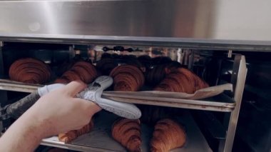 Baker taze pişmiş badem dolgulu kruvasanları fırından çıkarır. Fırın