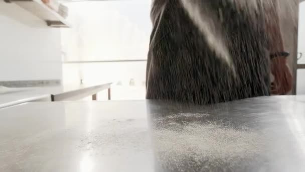 Пекарь посыпать муку на стол из нержавеющей кухни, чтобы сделать хлебобулочные изделия. Производство выпечки — стоковое видео