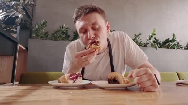 Homme européen mangeant appétissant croissant frais avec remplissage de chocolat dans un café. — Video