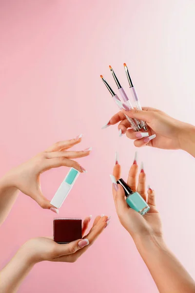 Vrouwelijke handen houden nagellak, borstels en andere manicure producten op een roze achtergrond. Catalogus foto — Stockfoto