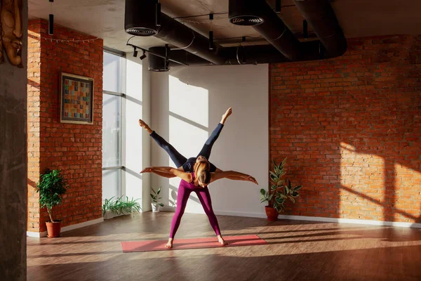 Paryogasana. Unga flickor i sport uniformer gör vackra par asana i rymliga yoga studio — Stockfoto