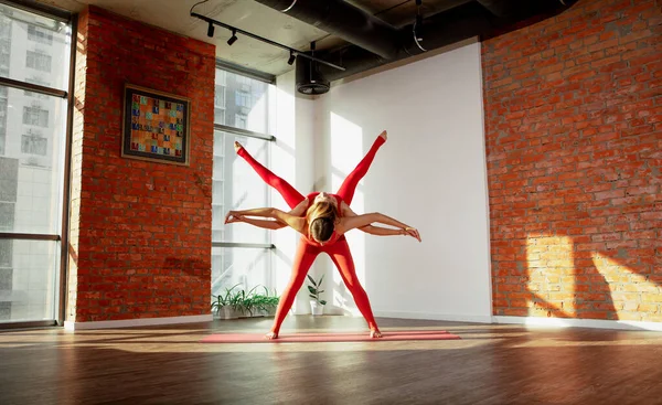 Paryogasana. Unga flickor i sport uniformer gör vackra par asana i rymliga yoga studio — Stockfoto