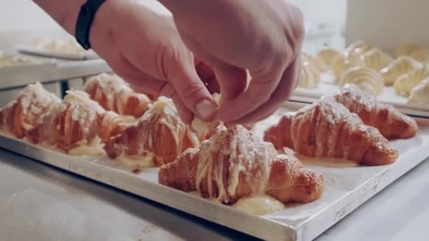 Croissant med mandelflingor. Baker dekorerar färska gyllene croissanter med mandel flingor — Stockvideo