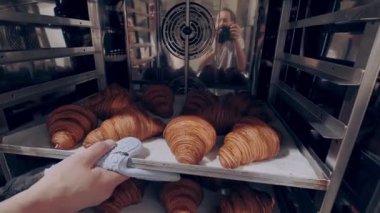 Baker taze pişmiş badem dolgulu kruvasanları fırından çıkarır. Pişirme süreci