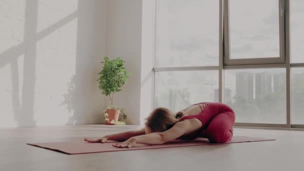 Hermoso yoga. Mujer joven en uniforme deportivo rojo se estira la espalda. concepto de estilo de vida saludable — Vídeos de Stock